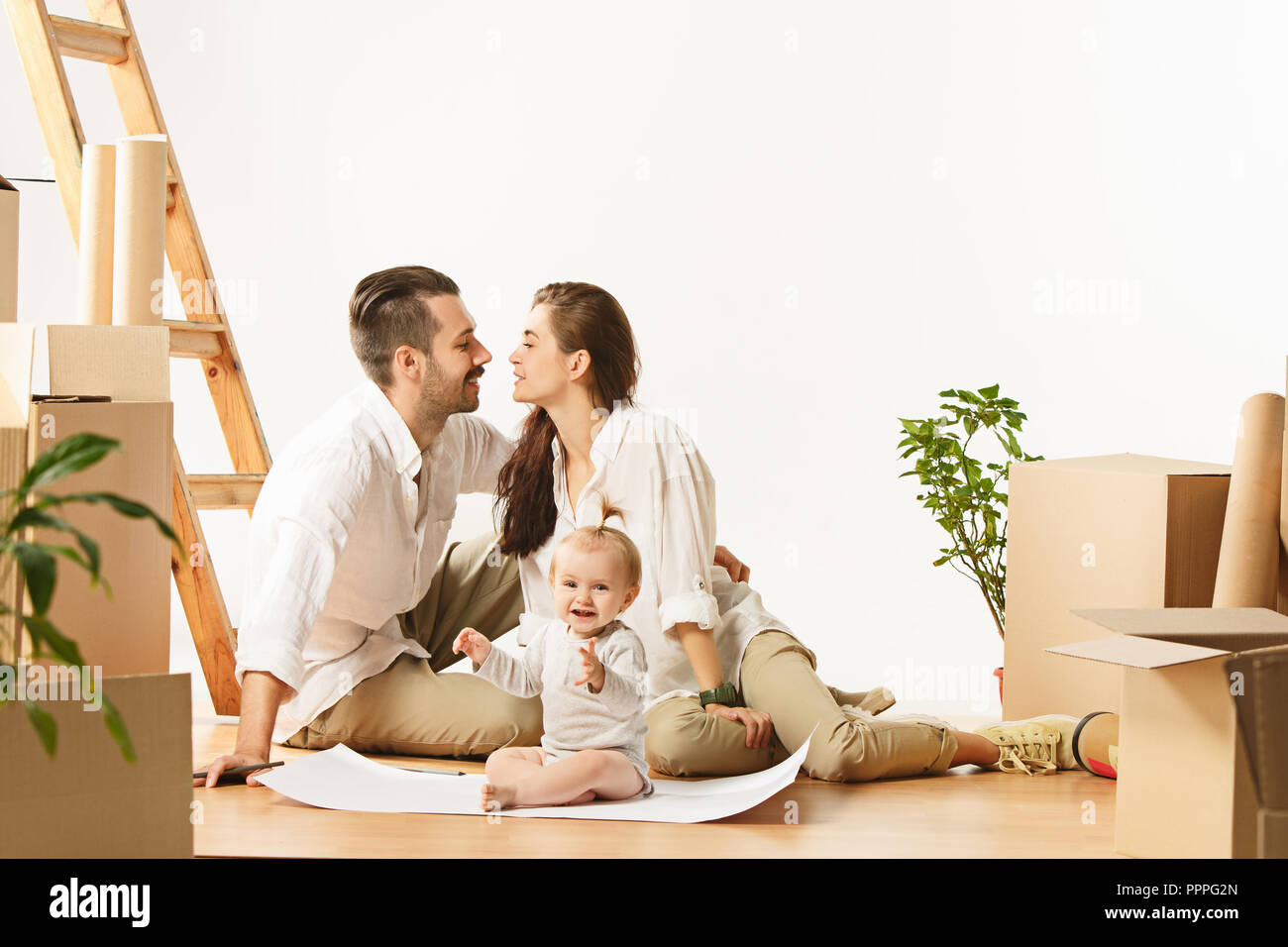 Paar in ein neues Zuhause. Glücklich Verheiratete mit neugeborenen Kind kaufen eine neue Wohnung leben zusammen zu beginnen. Die Familie bei Reparatur- und Umzug Planung zur Unterkunft gegen Boxen Stockfoto