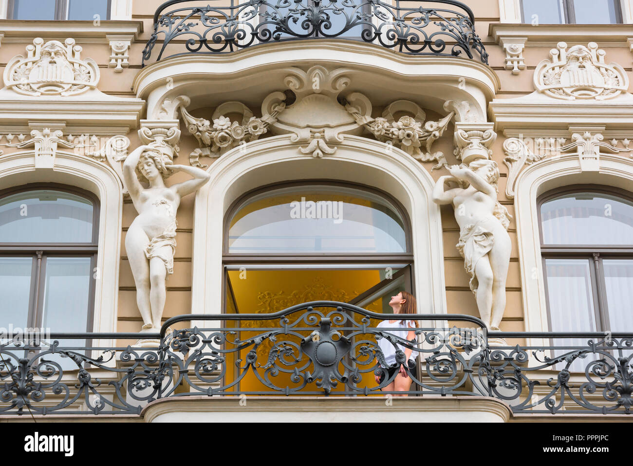 Riga Jugendstil Architektur, eine junge Frau auf einem Balkon in Elizabetes Iela im Art Nouveau Stadtteil von Riga sucht in einem der beiden Karyatiden. Stockfoto