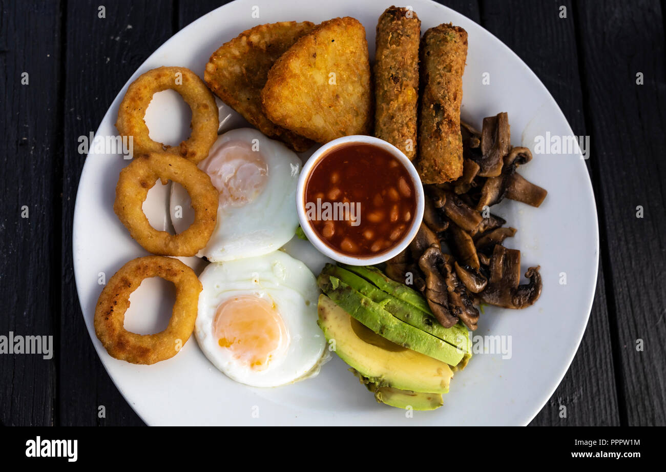 Nahaufnahme einer vegetarischen Englische Frühstück mit Bohnen in Tomatensoße, Spiegelei, Zwiebelringe, Ofen gebackenes Gemüse, Pilze und Avocado. Stockfoto
