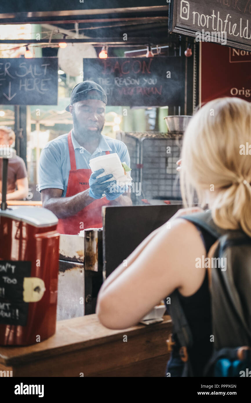 London, UK - 17. September 2018: Frau wartet auf ihr Essen in Northfield Metzgerei stand in Borough Markt, Personal kochen im Hintergrund. Borough M Stockfoto