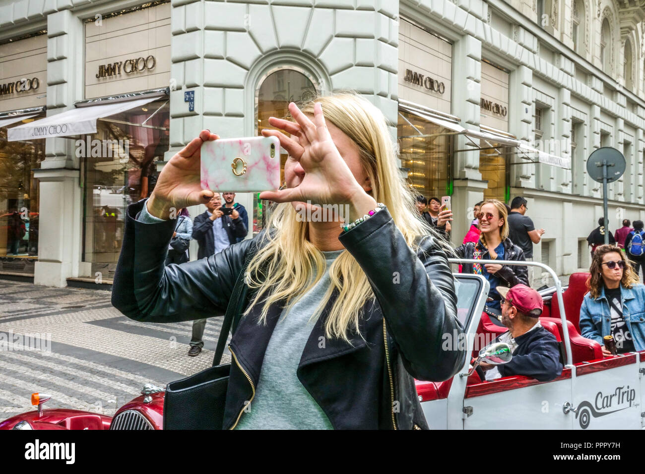 Junge Frau, die am Telefon vor dem Luxusgeschäft Jimmy Choo in der Parizska Straße, Prag, Tschechische Republik fotografiert Stockfoto