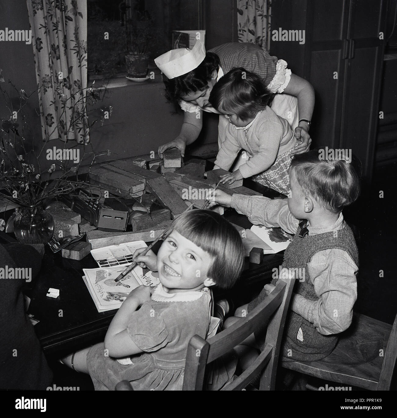 1950 s, historischen, nach dem Zweiten Weltkrieg Großbritannien und eine Krankenschwester helfen, drei kleine Kinder spielen mit Holz- Ziegel und Malerei in einer Ecke in einem Krankenhaus. Stockfoto