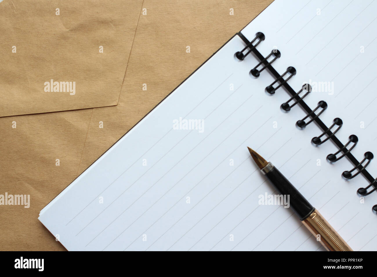 Ein Notebook mit sauberer Bettwäsche, einen Umschlag und eine Goldene Feder auf dem Tisch Stockfoto