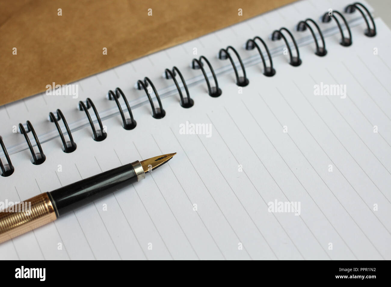 Ein Notebook mit sauberer Bettwäsche, einen Umschlag und eine Goldene Feder auf dem Tisch Stockfoto