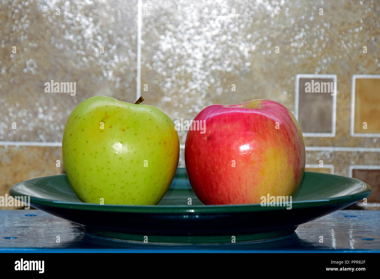 Beschmutzt, gelblich grün und gestreift gelblich-rote Äpfel auf einem grünen Schild an einem türkisfarbenen Tisch gelegt, horizontale Ansicht mit abstrakten Hintergrund Stockfoto