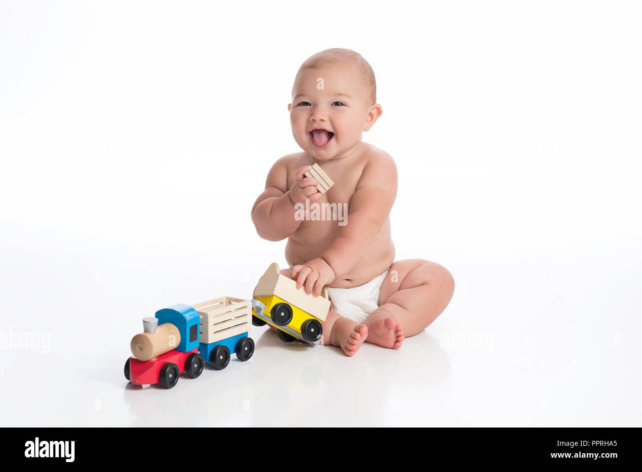 Ein lächelndes sieben Monate alten Baby Junge spielt mit einem hölzernen Zug. Im Studio auf einem weißen, nahtlose Kulisse erschossen. Stockfoto