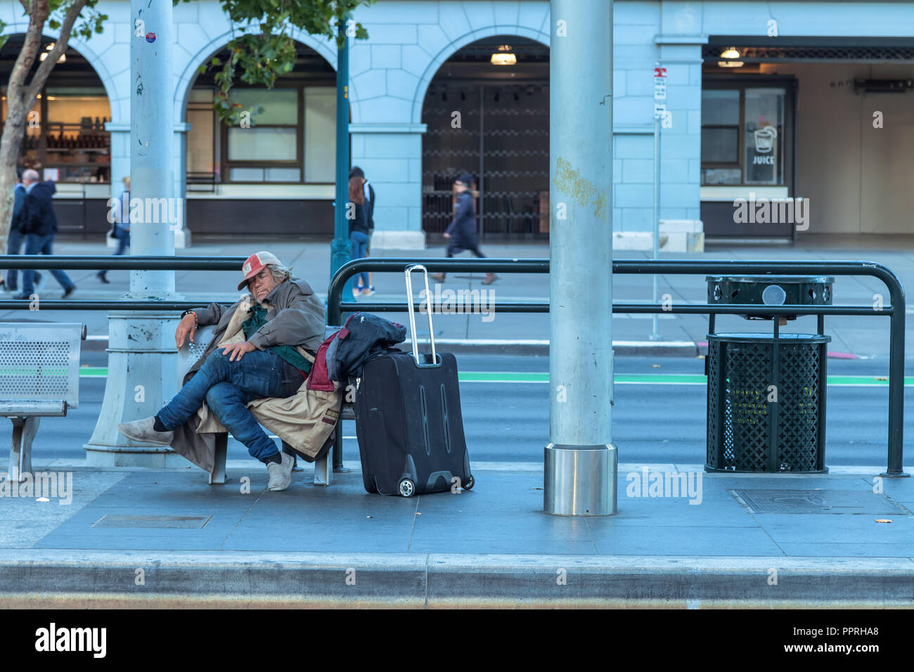 Ein obdachloser Mann mit seinem Eigentum auf einer Bank auf dem Bahnhof in San Francisco, Kalifornien, USA Stockfoto