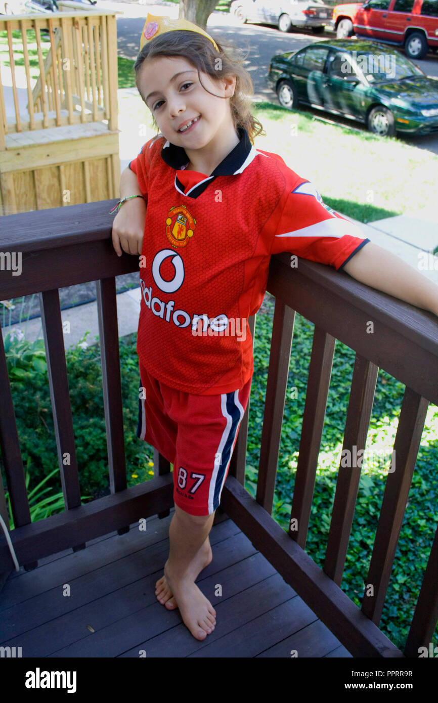 Junges Mädchen Alter 8 steht stolz auf Ihrer Veranda vor dem Tragen eines Manchester United mit dem Sponsor Vodafone cymbal Uniform. Chicago Illinois IL USA Stockfoto