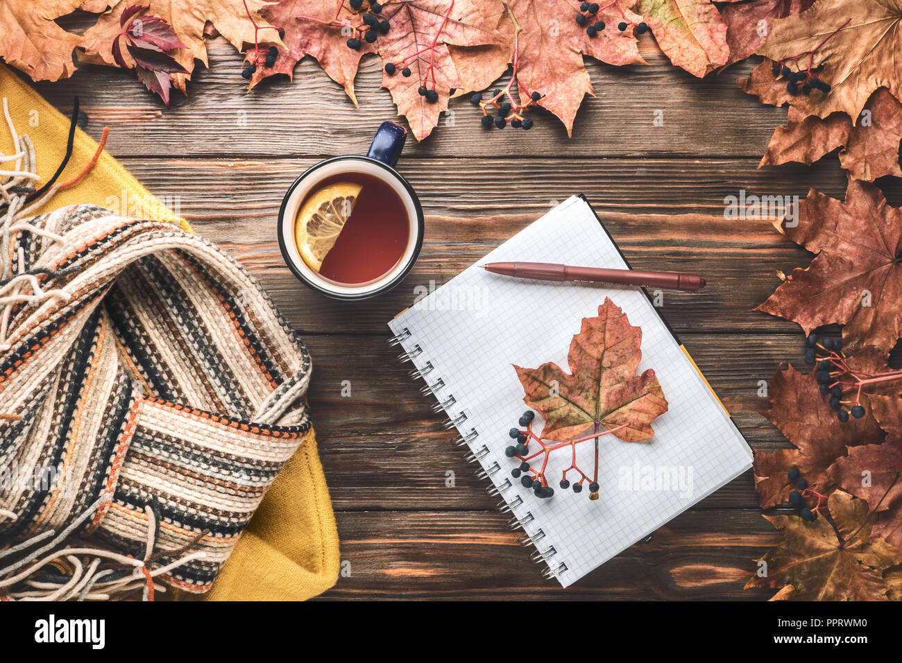 Herbst Mode saisonale Konzept gelb warm weicher Pullover skandinavischen Strickschal Tasse heißer schwarzer Tee Kaffee Fallen gefallen Ahornblätter auf hölzernen Tisch Stockfoto