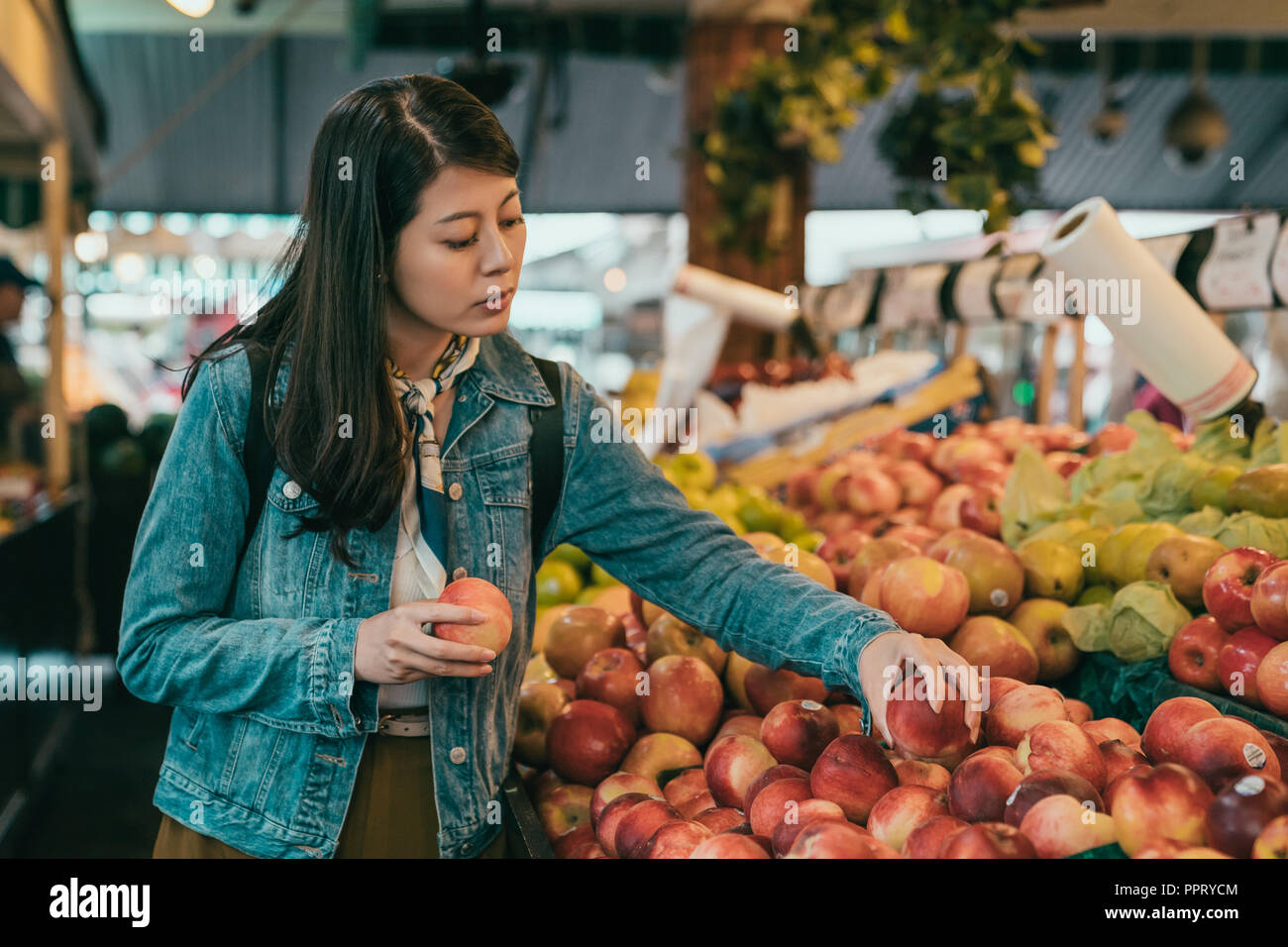 Junge Frau Äpfel pflücken in der ursprünglichen Bauernmarkt, vergleicht sie zwei Äpfel und gehen zurück auf das Regal zu stellen Stockfoto