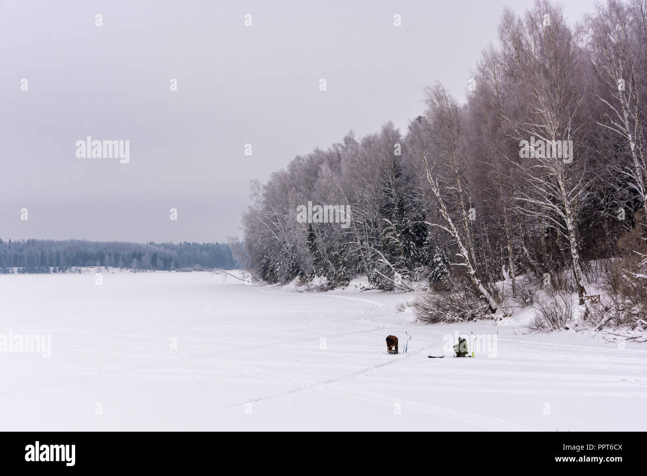 Zwei Fischer auf dem Eis angeln am großen Fluss an einem kalten Tag. Stockfoto