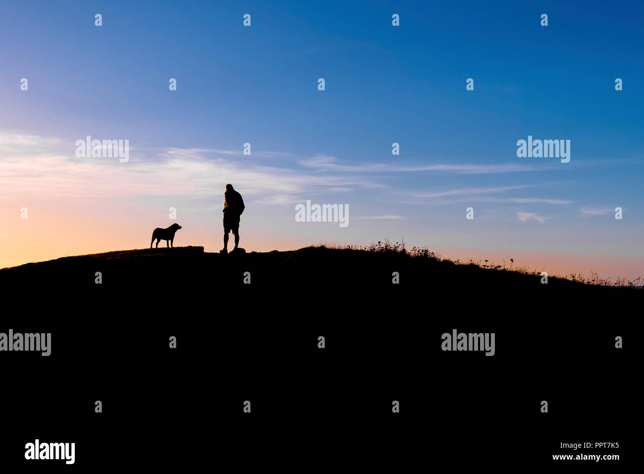 Ein Mann und sein Hund in Silhouette gegen einen farbenprächtigen Sonnenuntergang in Newquay in Cornwall gesehen. Stockfoto