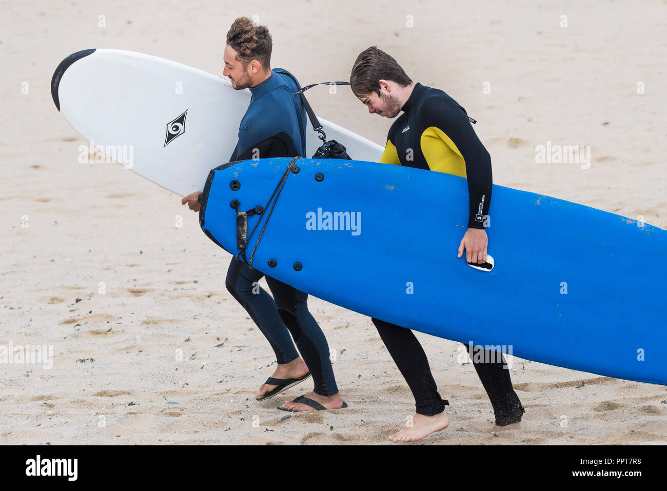 Zwei Surfer kämpfen ihre Surfbretter in starker Wind weht über den Fistral Beach in Newquay in Cornwall zu tragen. Stockfoto