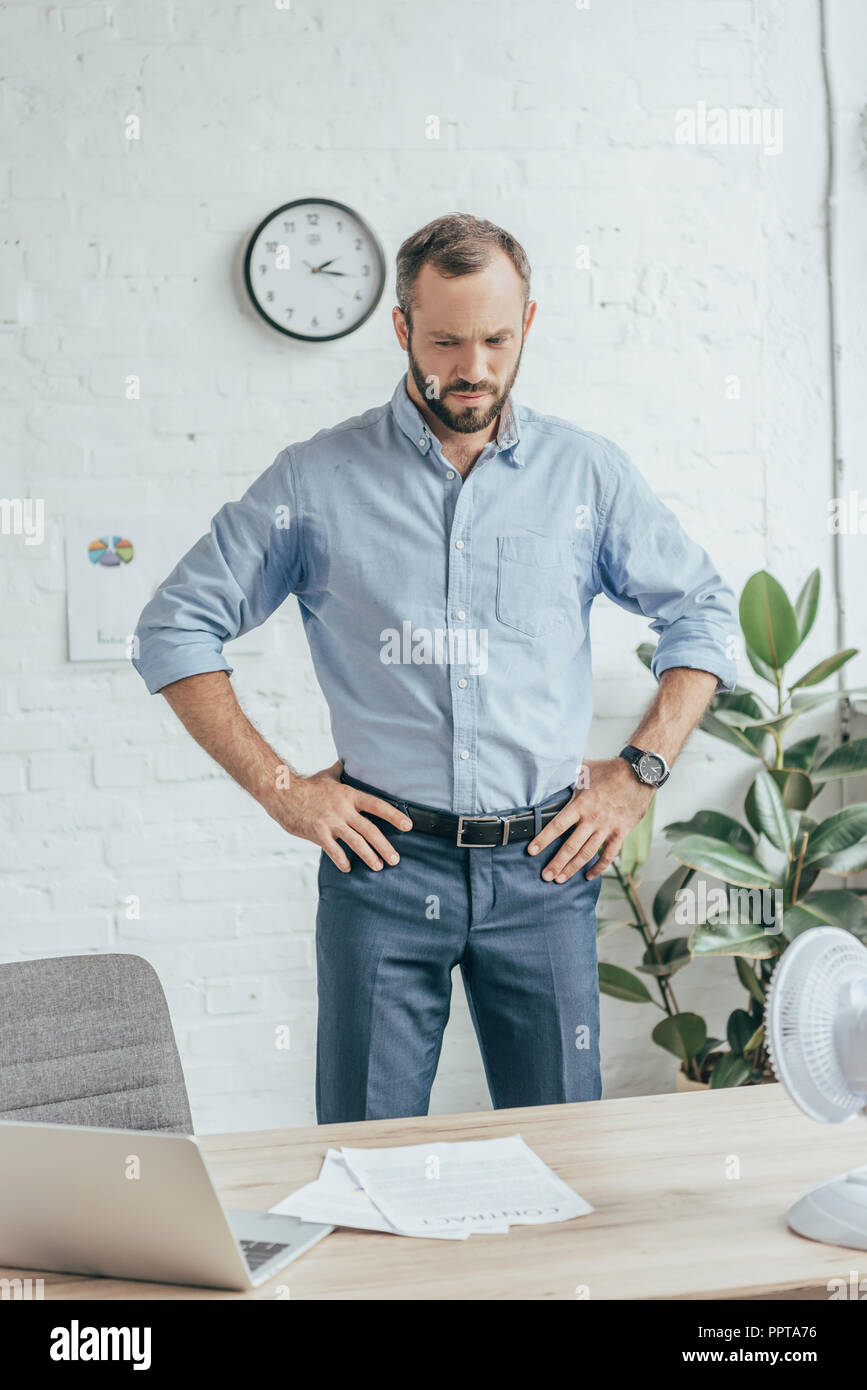 Verschwitzte Geschäftsmann in wet Shirt stehen im Büro mit Laptop, Unterlagen und elektrischer Ventilator Stockfoto