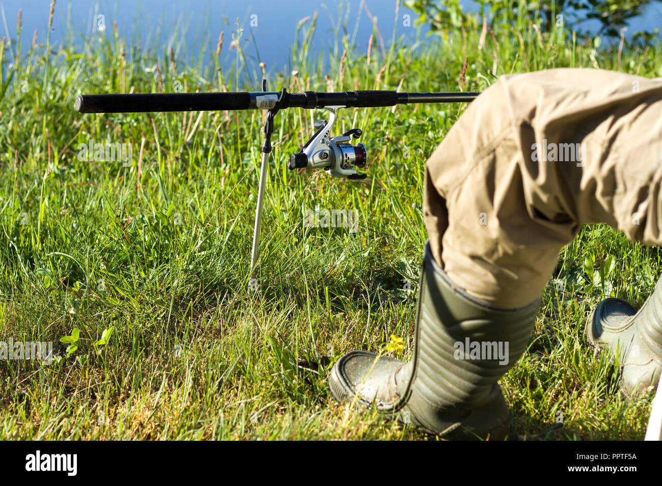 Angler's Bein in Gummistiefeln gegen die Wiese und Wasser. Erdungsstange, montiert auf einem Rack Stockfoto