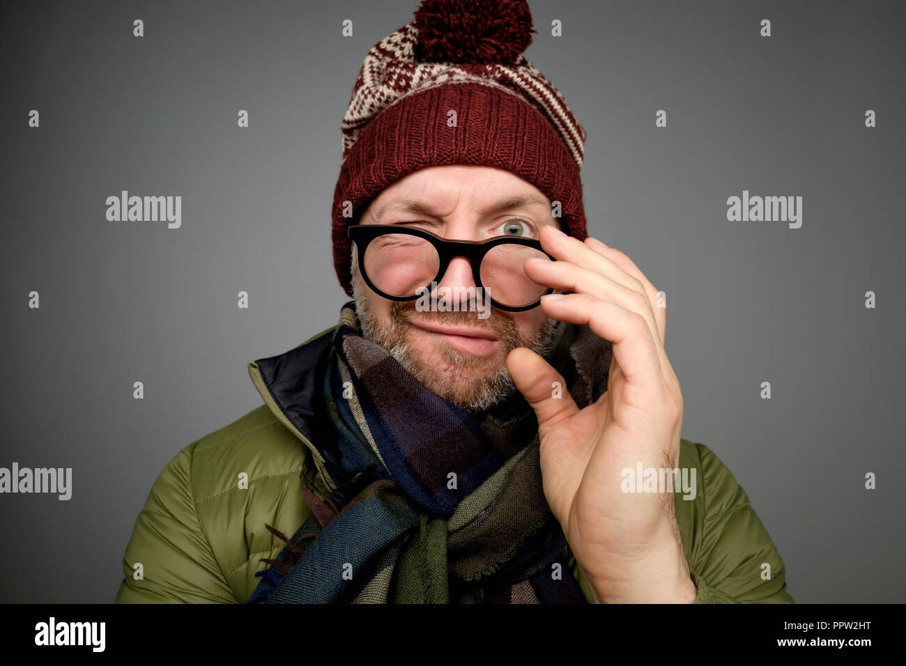 Porträt eines lustigen reifer Mann in warme Winterkleidung an Kamera durch Gläser über grauer Hintergrund suchen. Stockfoto
