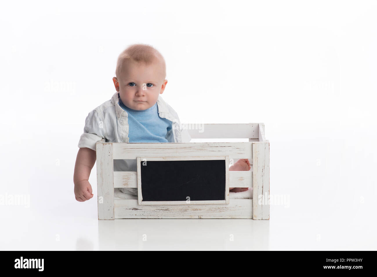 Ein sieben Monate altes Baby boy in eine weiße Tafel Kiste sitzen. Im Studio auf einem weißen, nahtlose Kulisse erschossen. Stockfoto