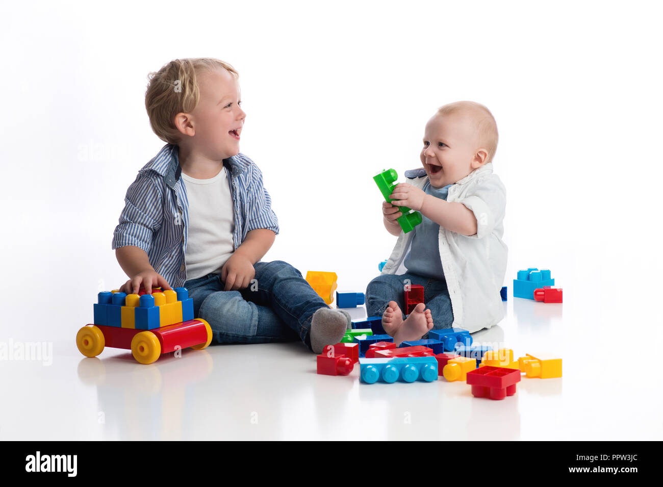 Ein zwei Jahre alter Junge spielt mit seinen sieben Monate alten Baby Bruder spielen mit Bausteinen. Im Studio auf einem weißen, nahtlose Kulisse erschossen. Stockfoto Ein zwei Jahre alter Junge spielt mit seinen sieben Monate alten Baby Bruder spielen mit Bausteinen. Im Studio auf einem weißen, nahtlose Kulisse erschossen. Stockfoto