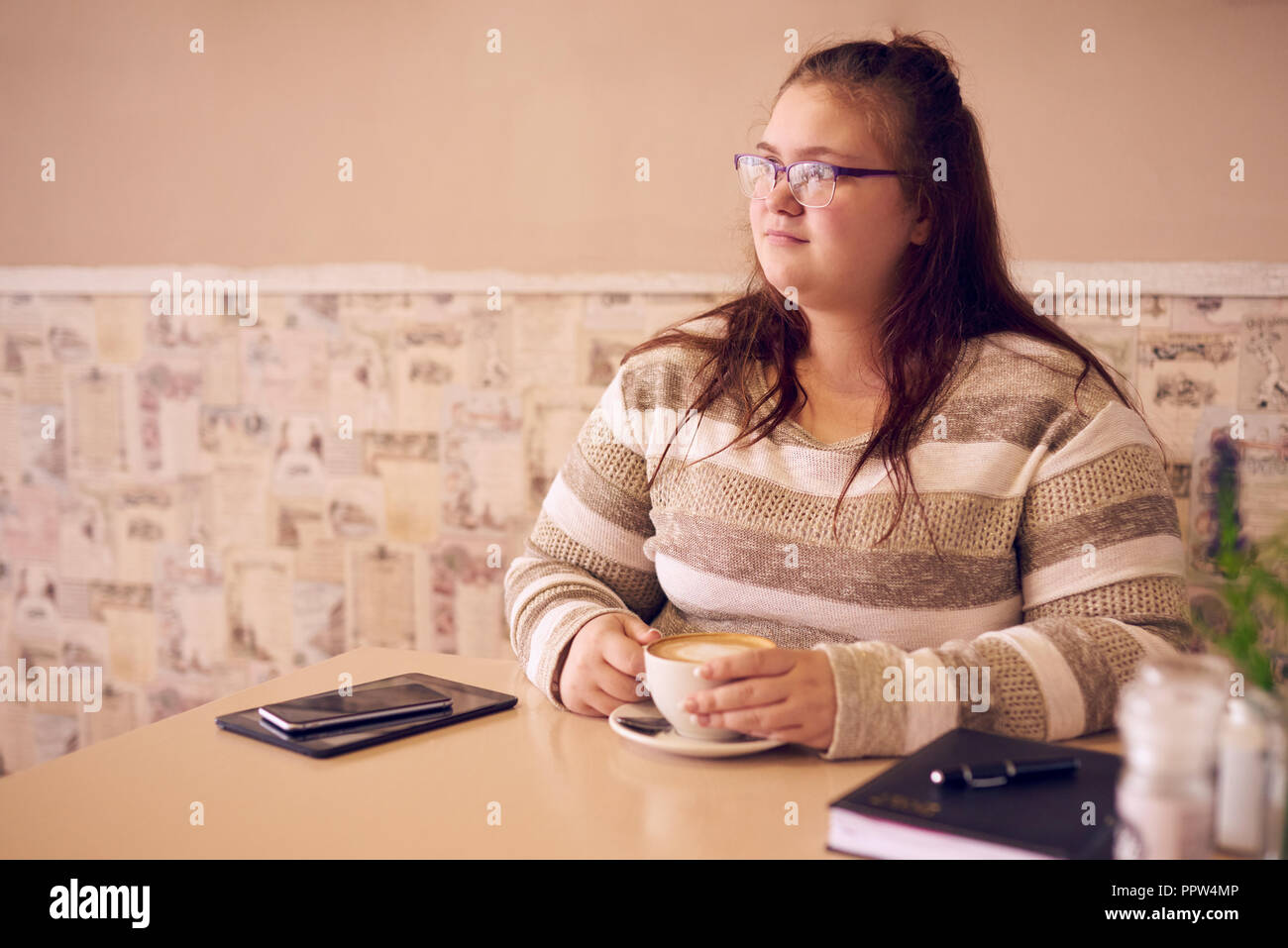 Übergrößen Frau sitzt in einem hellen Café, während Sie bei einer Tasse Kaffee ihre Hände warm halten und bereit mit Ihrem Tablet-PC auf dem Tisch weiter arbeiten können. Stockfoto