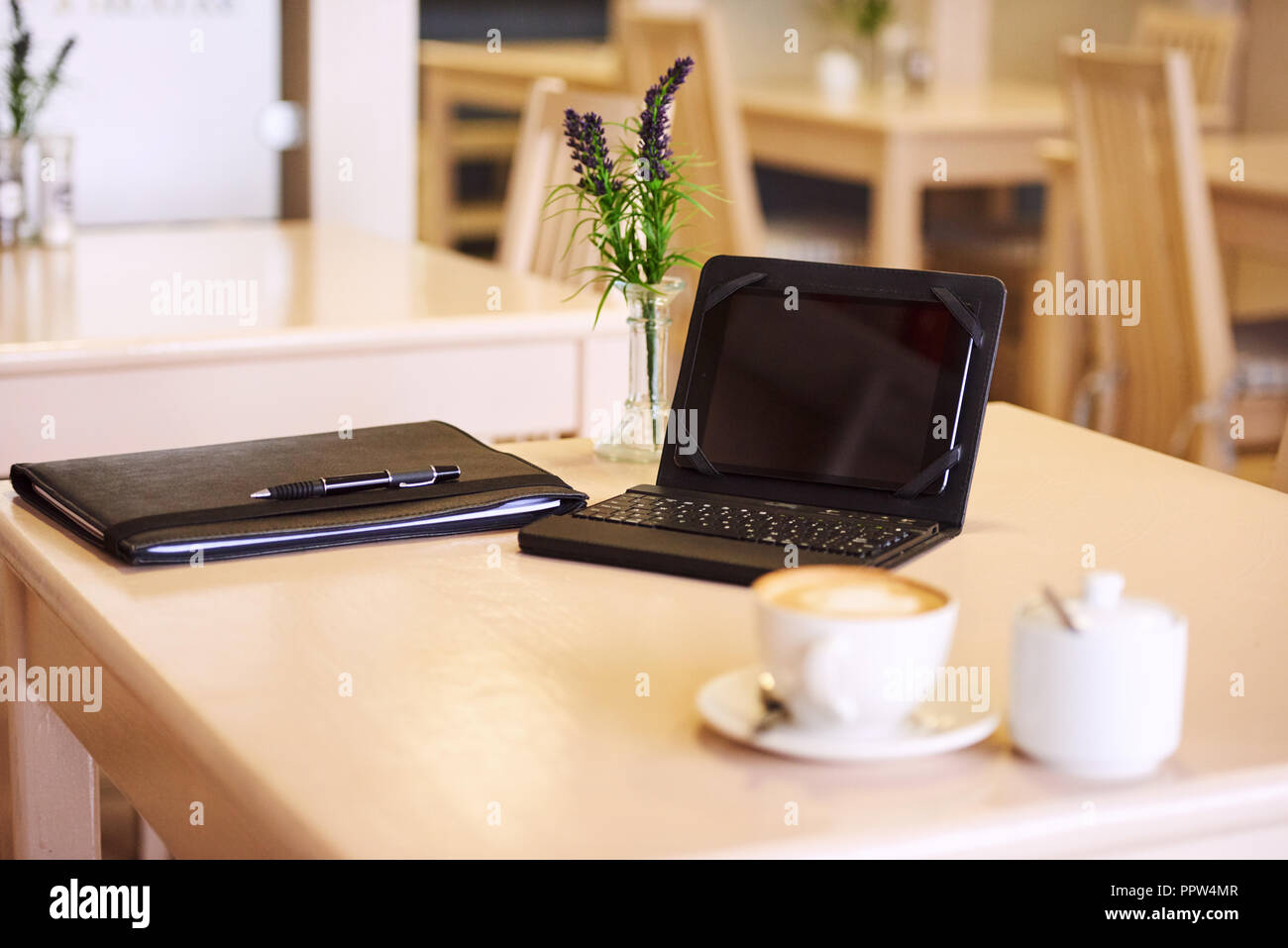 Elektronische Tablet und Tastatur einrichten am Tisch mit einem Notizblock und einige Kaffee sowie einem Lavendel center Stück auf einem hellen Sommermorgen. Stockfoto