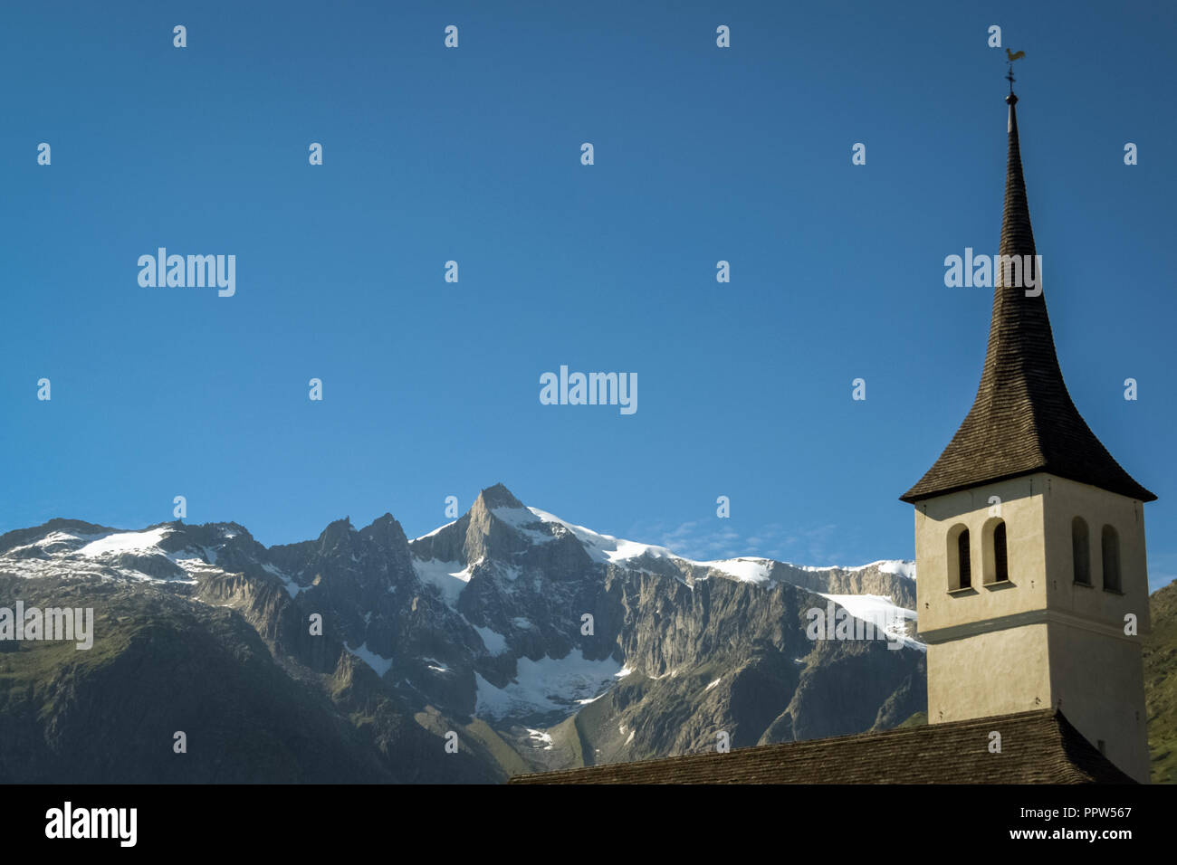 Mit Blick auf den Uhrturm der Kirche in Bellwald vor dem Hintergrund der großen Berge der Fischertal (Wallis, Schweiz) Stockfoto