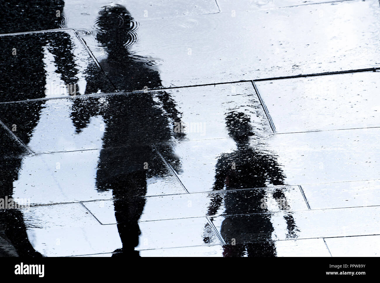 Unscharfe Reflexion Schatten Silhouette in eine Pfütze von Geschwistern und Eltern wandern nasse Straße der Stadt Stockfoto