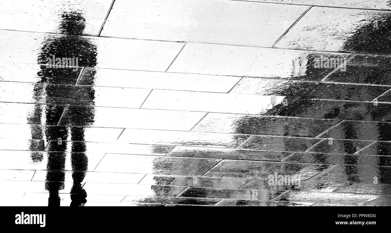 Unscharfe Reflexion Schatten Silhouetten von einem Mann zu Fuß auf dunklen regnerischen city street in Schwarz und Weiß Stockfoto