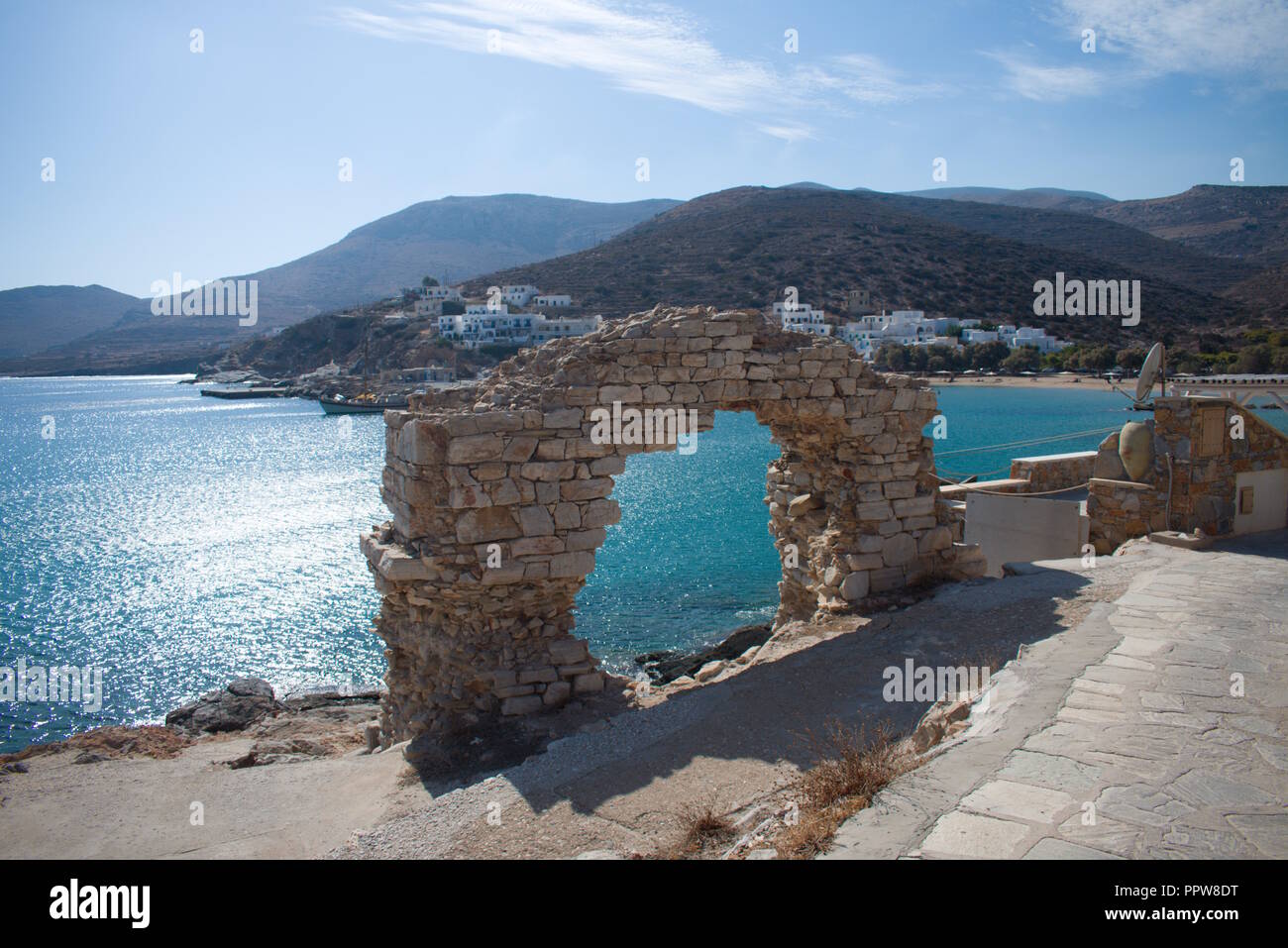 Blick auf ein zerstörtes Gebäude am Rande des Meeres auf der schönen griechischen Insel Sikinos. Das Sonnenlicht reflektiert sich auf dem ruhigen Wasser der Bucht. Stockfoto