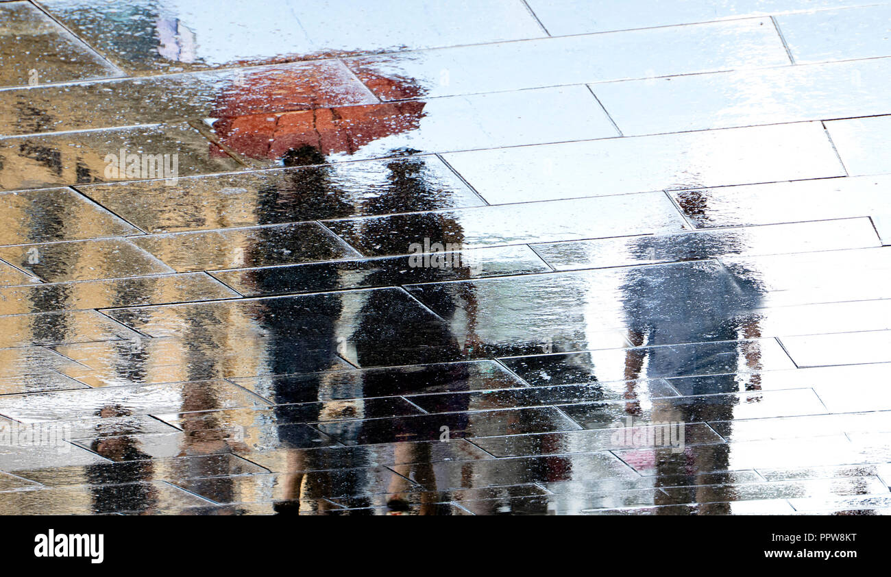 Unscharfe Reflexion Schatten Silhouette in eine Pfütze von Menschen zu Fuß regnerischen und sonnigen Stadt. Stockfoto