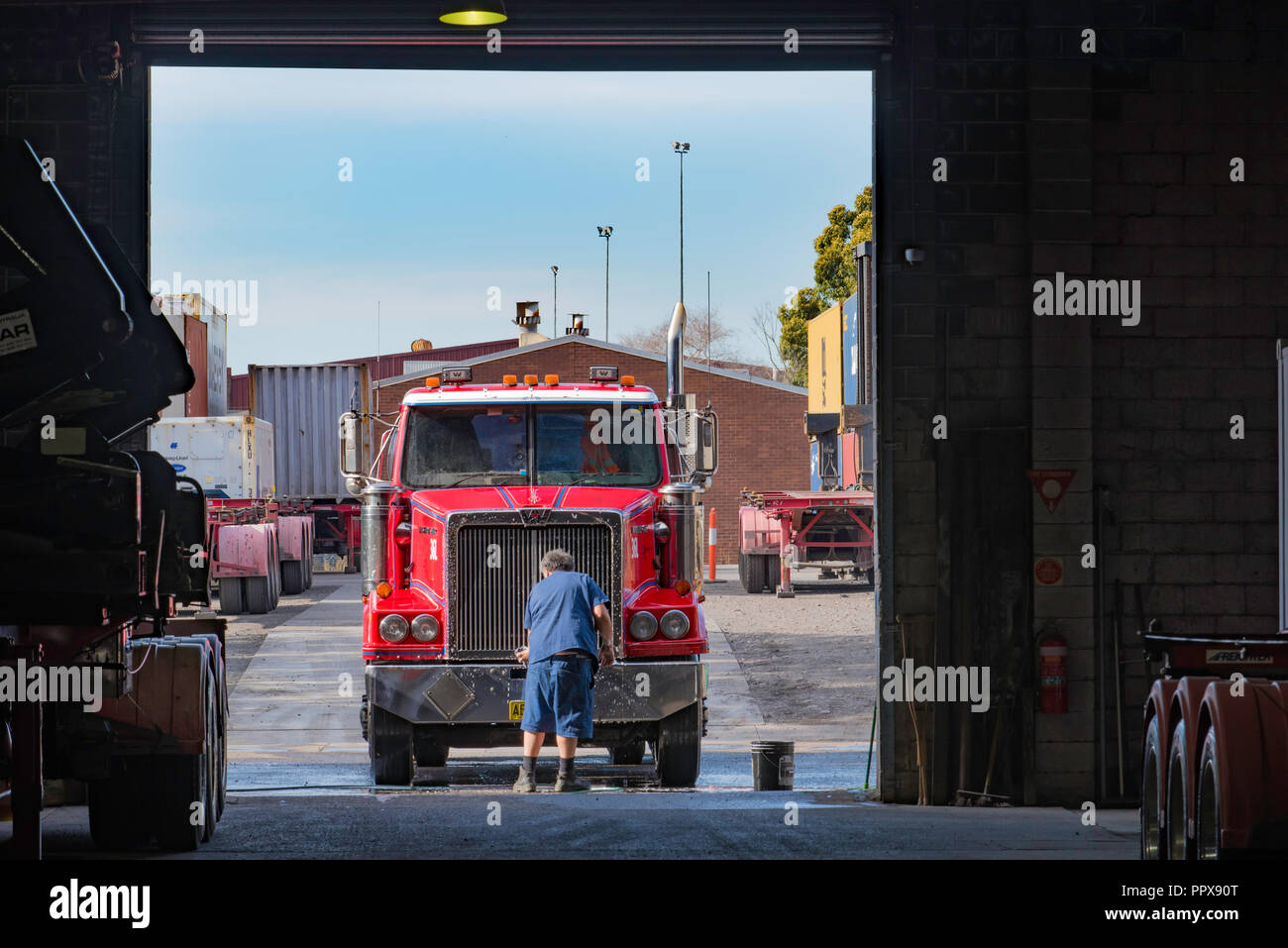 Eine australische LKW-Fahrer waschen Sie das vordere Ende eines roten Prime Mover, Auflieger, LKW-Flotte Hof, in einem Lager Eingang Stockfoto
