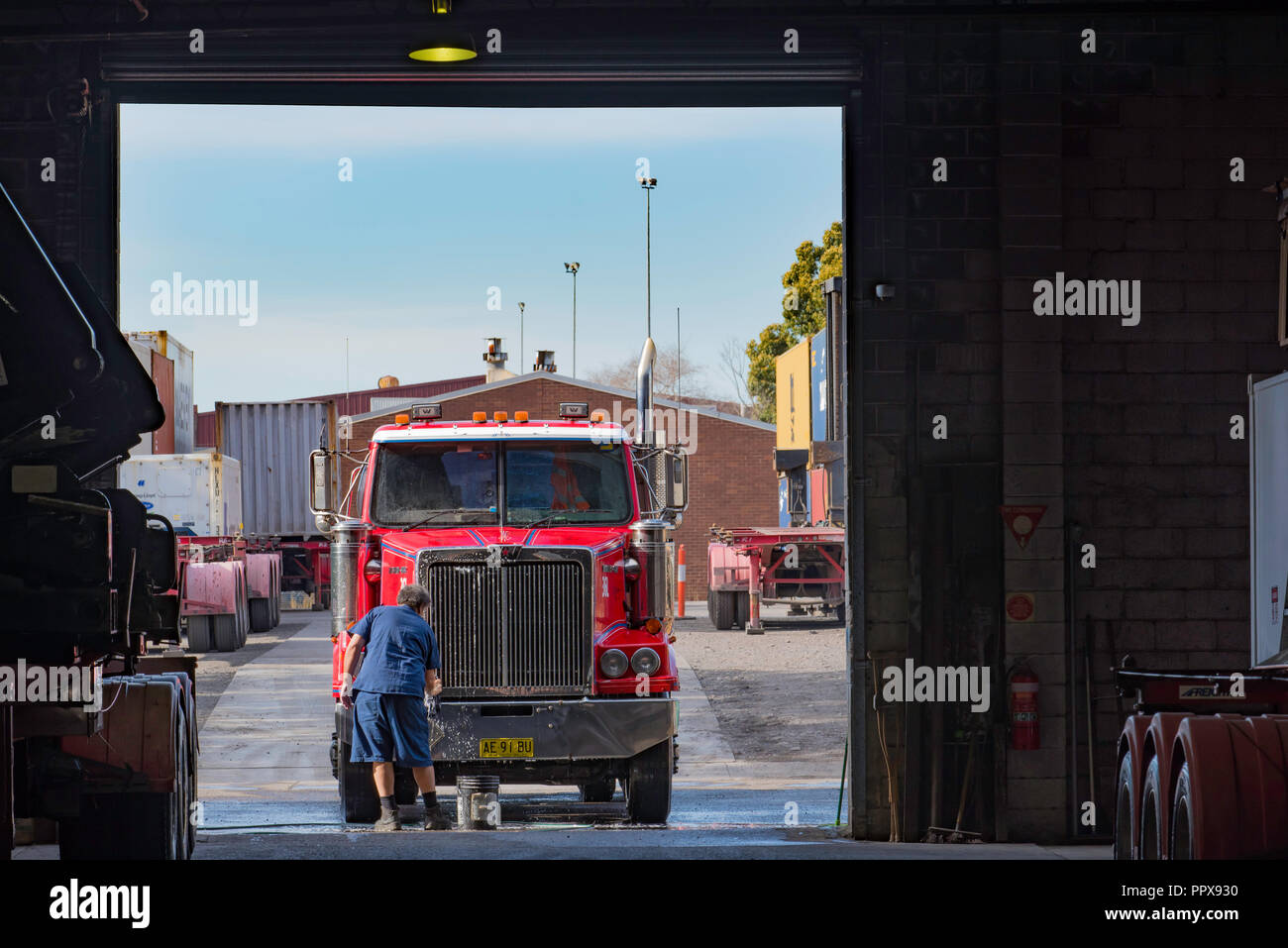 Eine australische LKW-Fahrer waschen Sie das vordere Ende eines roten Prime Mover, Auflieger, LKW-Flotte Hof, in einem Lager Eingang Stockfoto