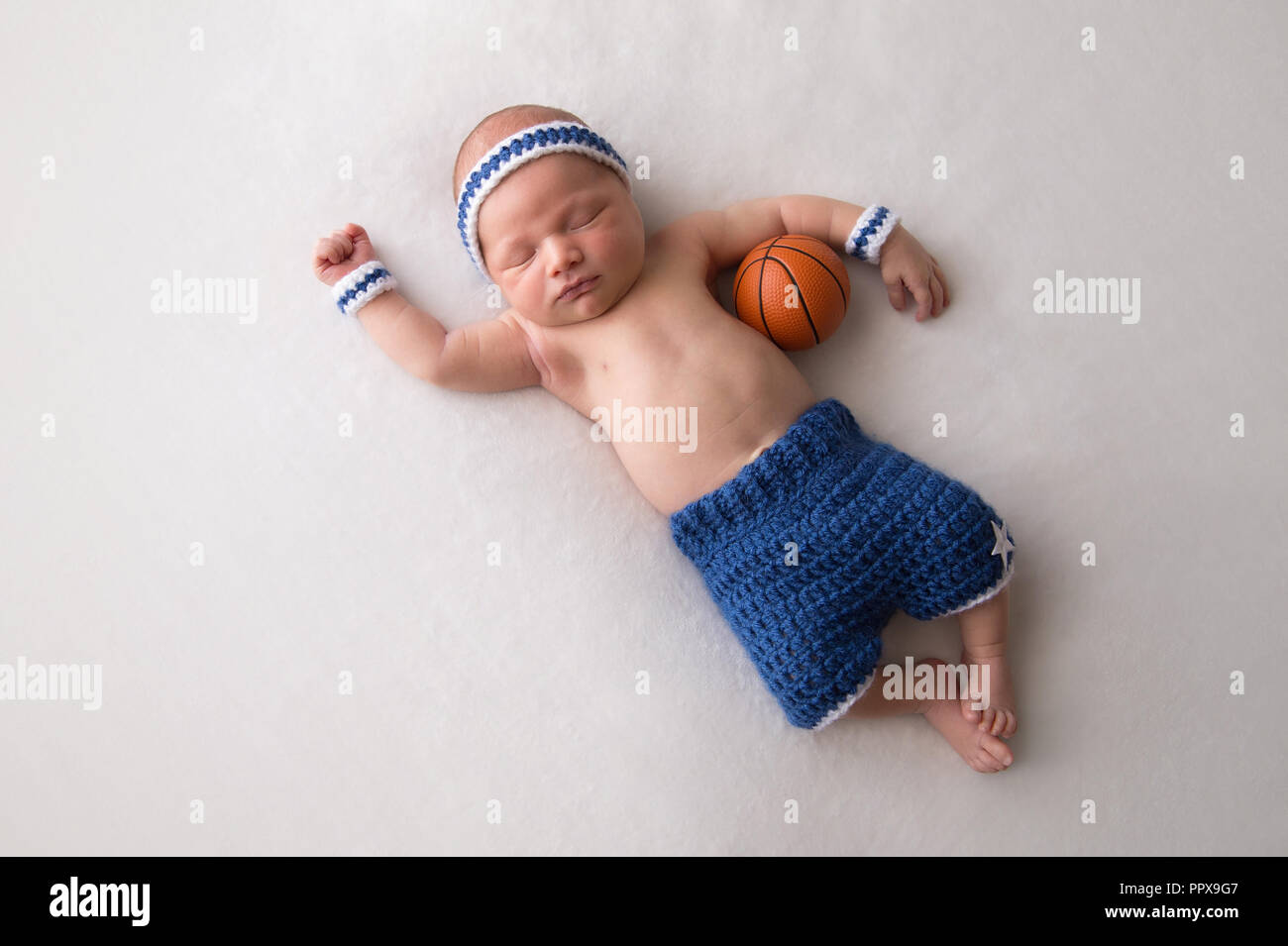 Zehn Tage alten Baby Boy tragen Basketball Shorts und SchweiB Bands. Er schlaft auf dem Rucken und hat einen winzigen Basketball in seinem Arm gelegen Stockfotografie Alamy