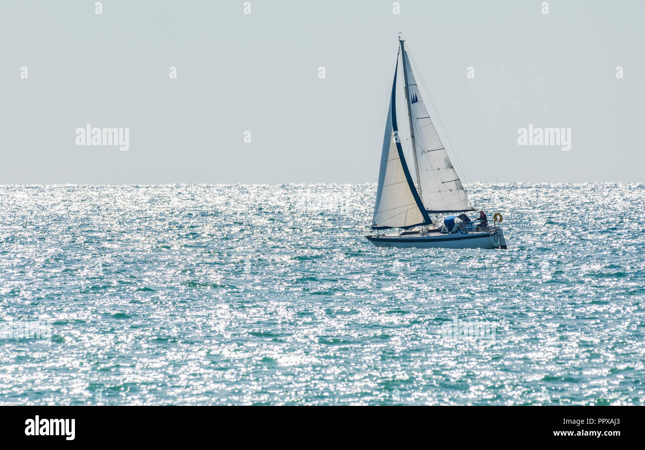 Einzelne person Yacht segeln auf See mit der Morgensonne funkelnden im Ozean, in Großbritannien. Stockfoto