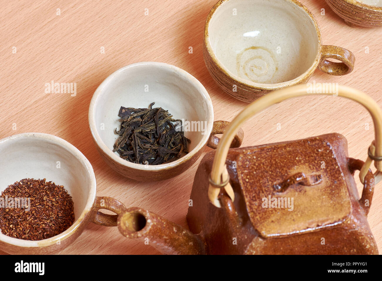 Tassen und Keramik Teekanne mit grüner Tee Blätter und rooibos. Es steht auf einem Holztisch. Stockfoto
