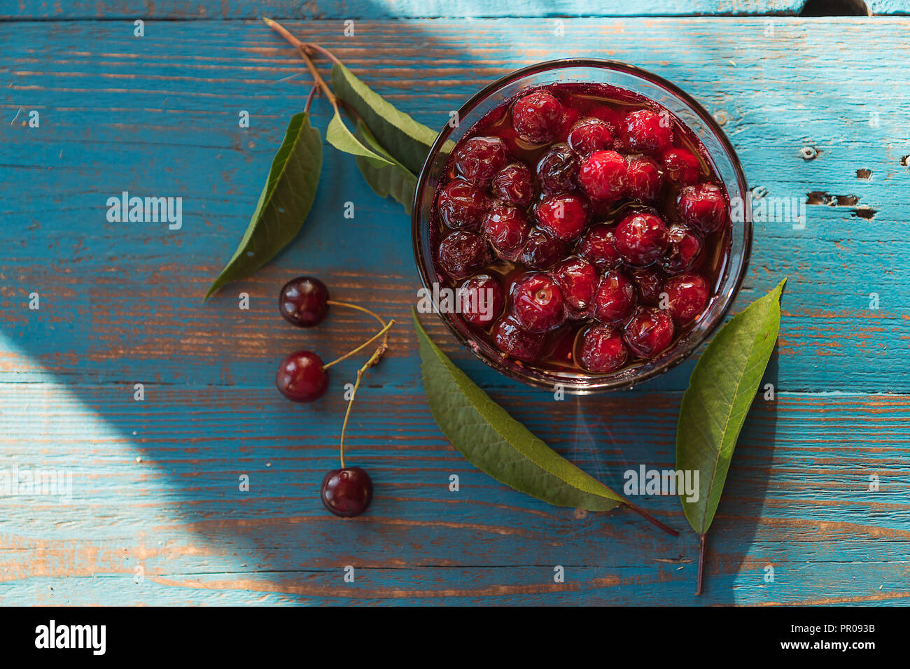 Cherry jam in Glasschale, über alte blaue Holztisch, Tageslicht, flach. Stockfoto