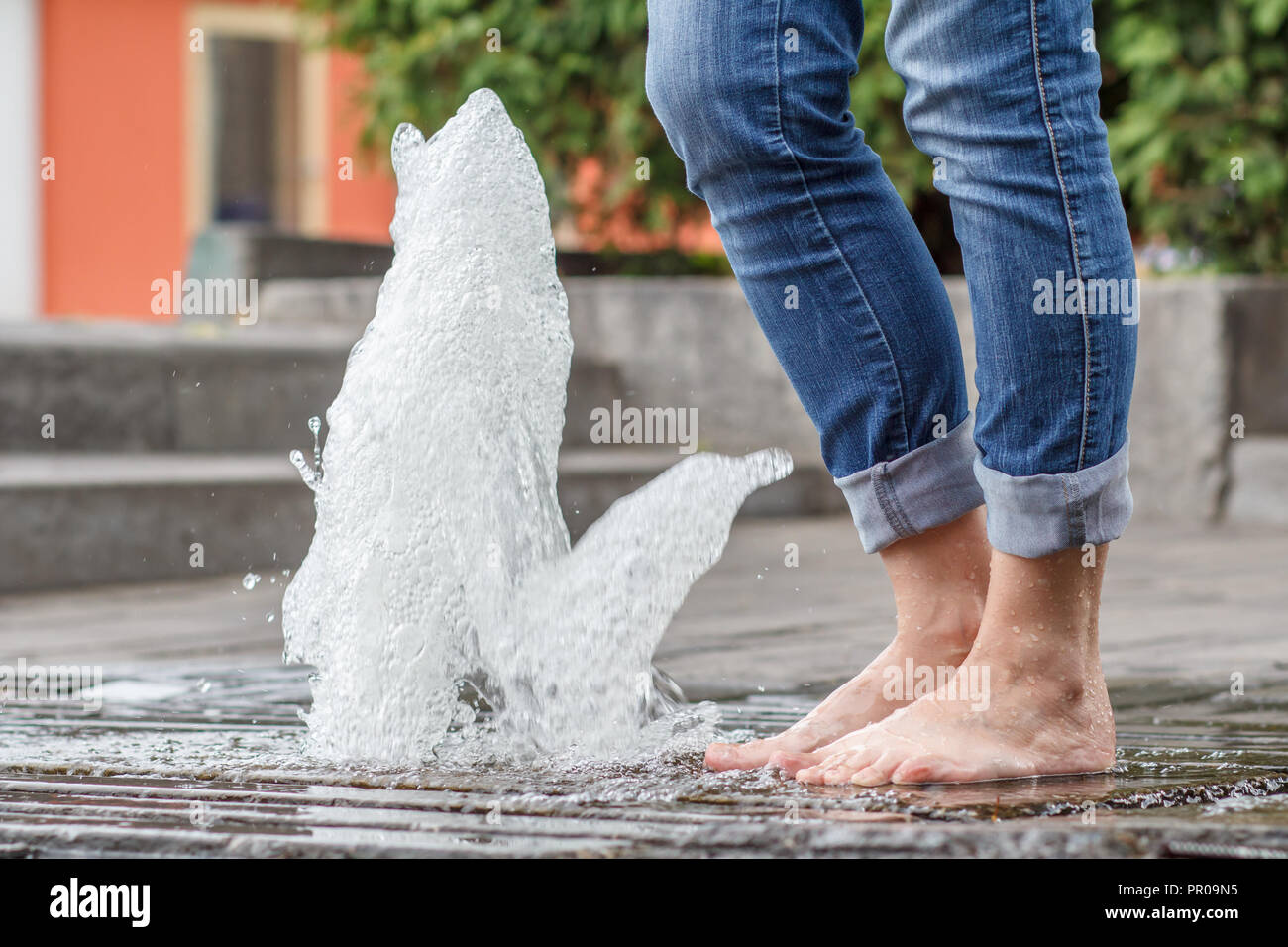 Füße der Frau in Jeans mit Tropfen Wasser auf ihnen in der Nähe der Brunnen. Sonnigen Tag im Sommer. Die Hitze entkommen Stockfoto
