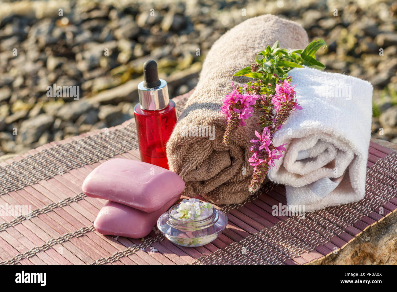 Schüssel mit Meersalz, Flaschen mit Aromaöl, Seife, wilde Blumen und Handtücher mit Bambus Tuch auf Steinen. Wellness Produkte auf natürliche Hintergrund Stockfoto