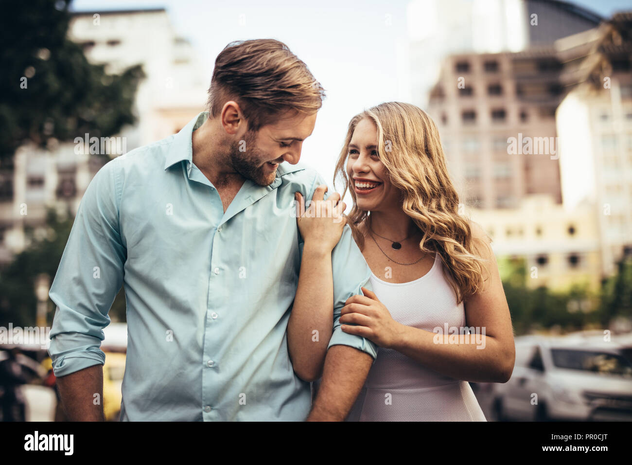 Lächelnde Frau zu Fuß auf der Straße mit ihrem Partner seine Hand. Paar in fröhlicher Stimmung zu Fuß auf der Straße zu suchen. Stockfoto