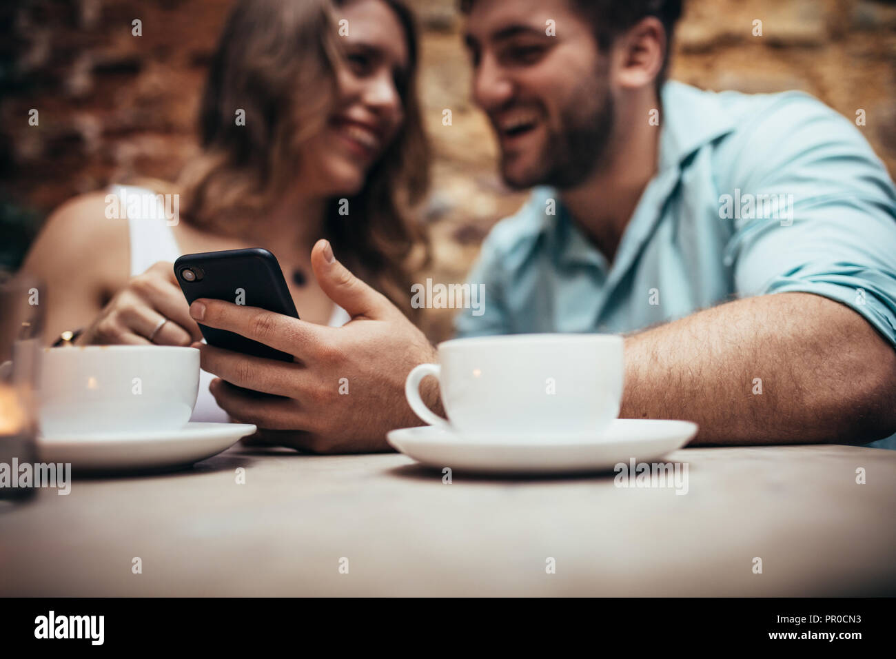 Lächelndes Paar im Coffeeshop Zeit miteinander zu verbringen. Mann in einem Restaurant mit seiner Freundin sitzen und mit Blick auf sein Mobiltelefon. Stockfoto
