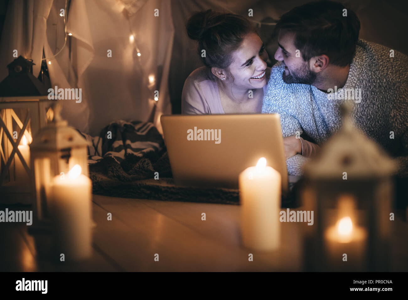 Lächelndes Paar auf dem Bett lag, an jedem anderen Suchen mit einem Laptop vor. Paar beim Film auf Laptop in der Nacht im Schlafzimmer mit Kerzen beleuchtet und t Stockfoto