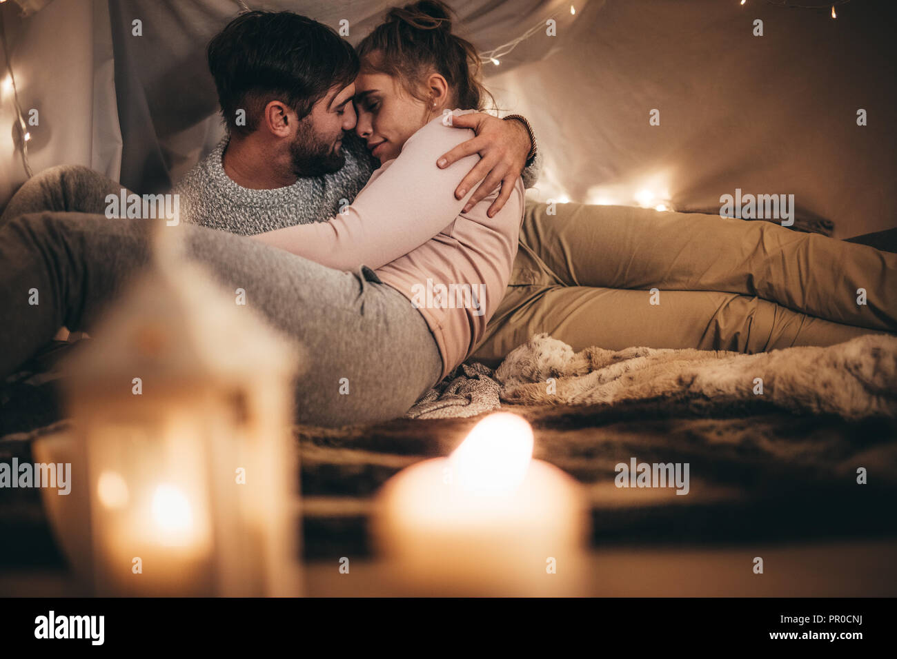 Frau auf dem Bett in die Arme ihres Ehemanns lag mit geschlossenen Augen. Paar romancing halten jedes andere im Schlafzimmer mit Kerzen brennen in den Vordergrund. Stockfoto
