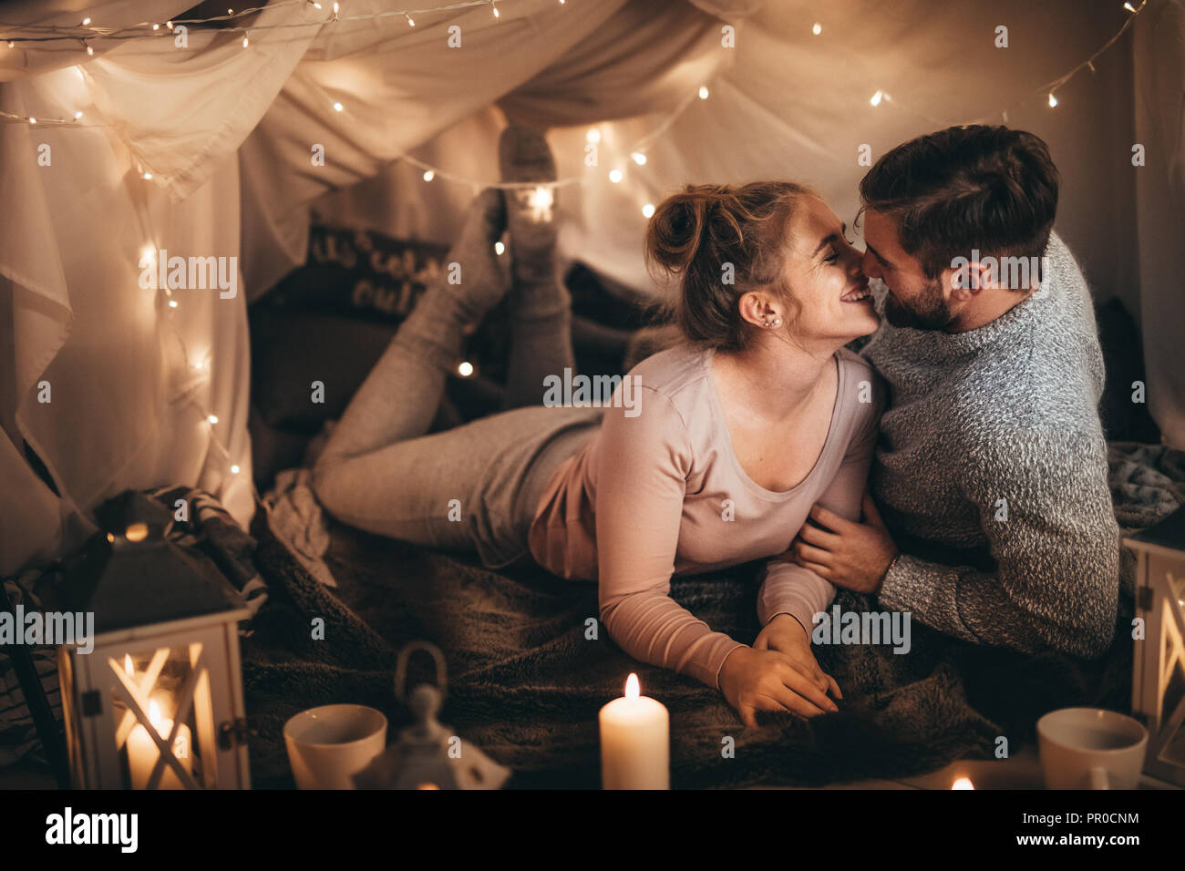Paar zusammen auf dem Bett in einem Zimmer mit Kerzenlicht und winzige serielle Lampen eingerichtet. Lächelnde Frau verbringt gerne Zeit mit ihrem Mann in Schlafzimmer Stockfoto