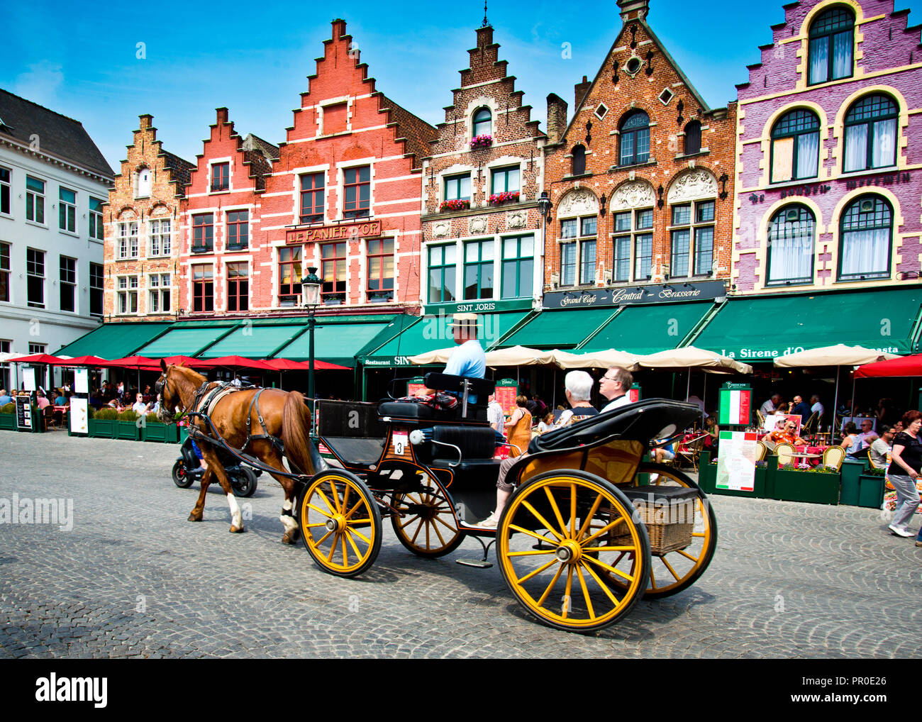 Touristen, die auf eine Stadttour in einer Pferdekutsche durch alte Gebäude genommen werden, jetzt Cafés und Restaurants mit verzierten Giebeln in der historischen Brügge, Stockfoto