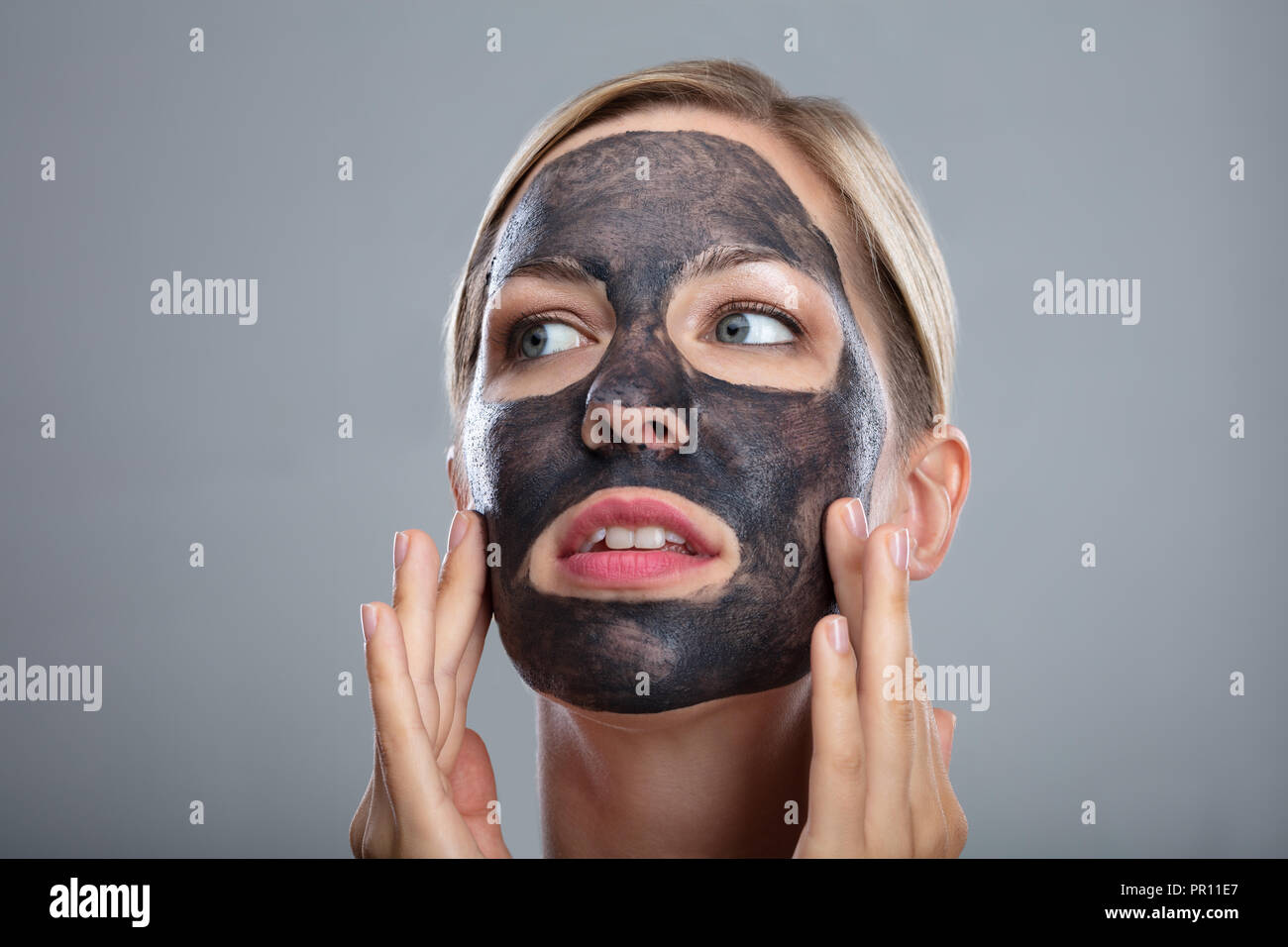 Close-up eine glückliche Frau mit Aktivkohle Maske auf grauem Hintergrund Stockfoto