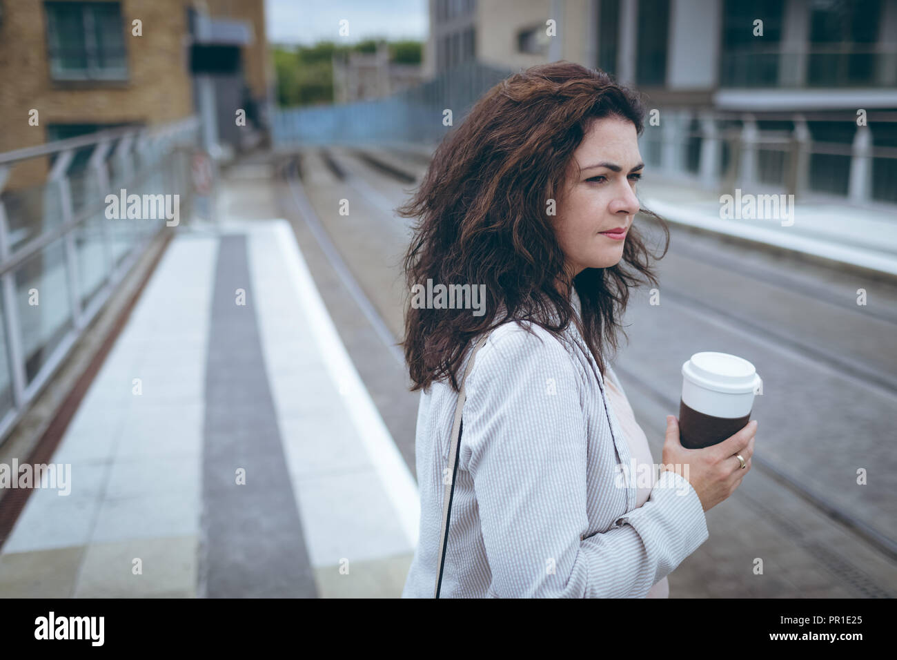 Mit Kaffeetasse stehen am Bahnhof Geschäftsfrau Stockfoto