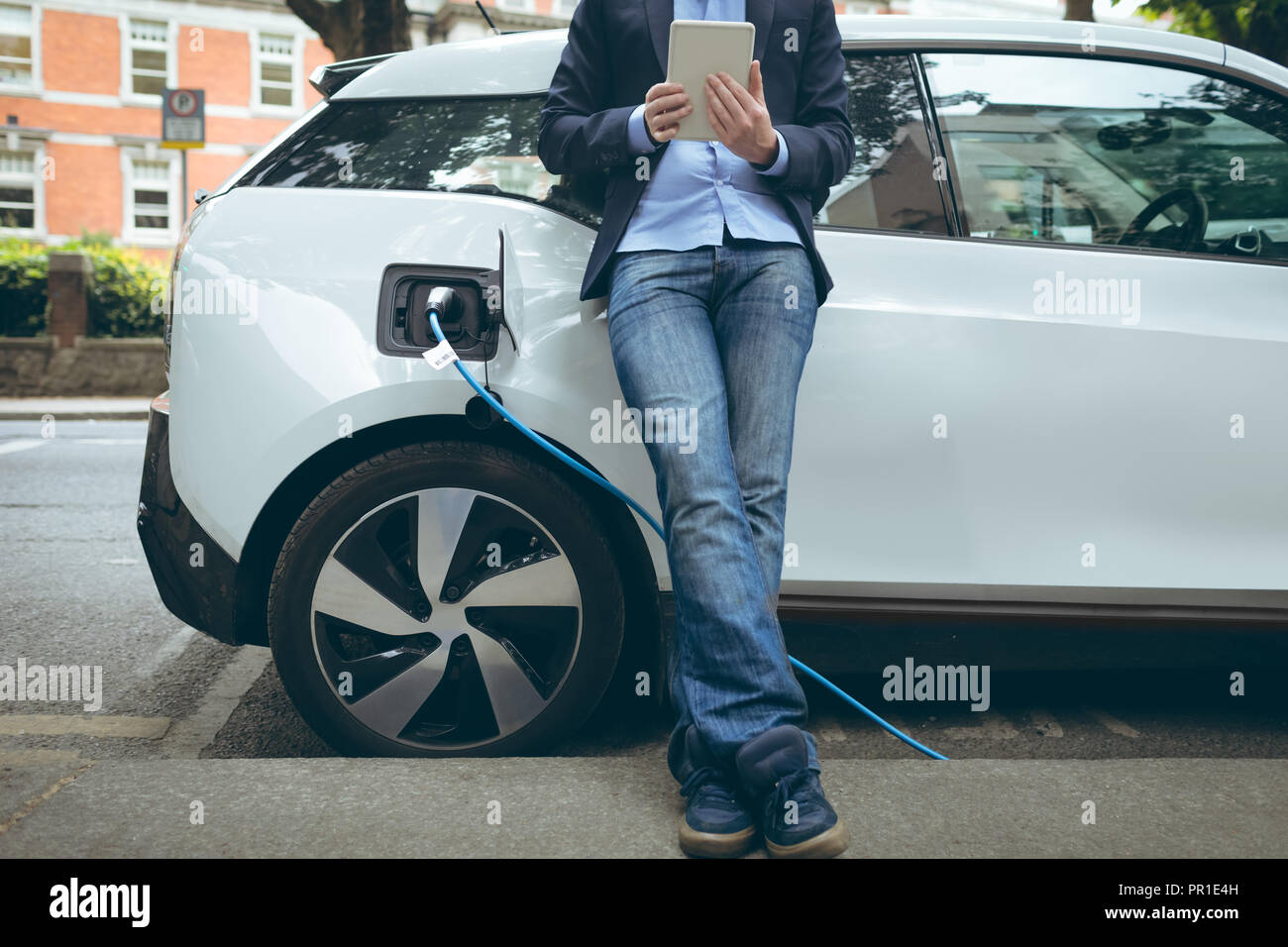 Mit digitalen Tablet während des Ladevorgangs Elektroauto an der Ladestation Geschäftsmann Stockfoto