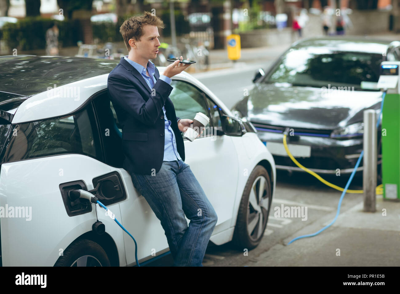 Unternehmer Gespräch am Handy während des Ladevorgangs Elektroauto Stockfoto