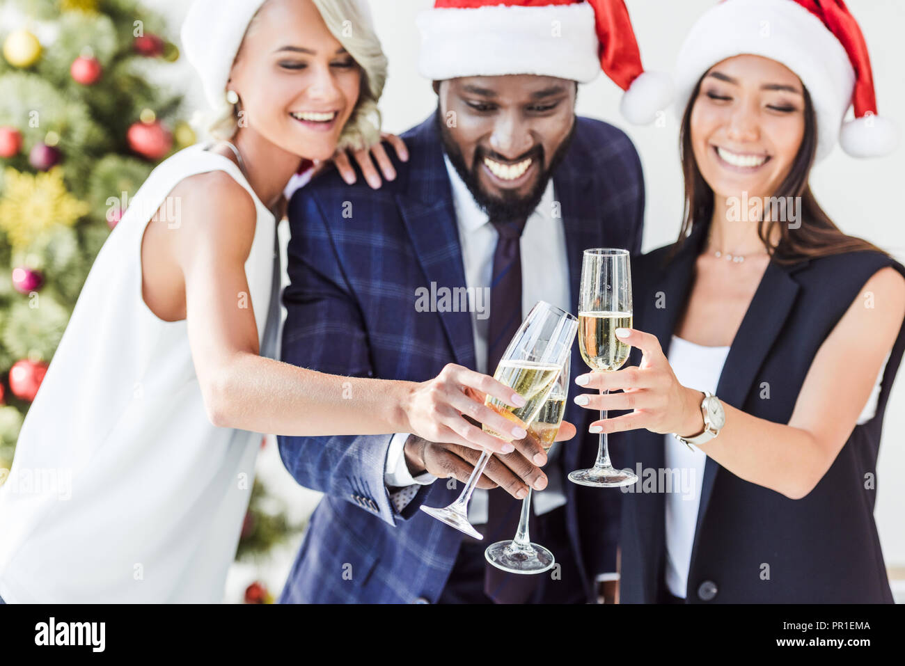 Lächelnd multiethnischen Geschäftsleute in santa Hüte klirren mit Gläser Champagner in Office Stockfoto