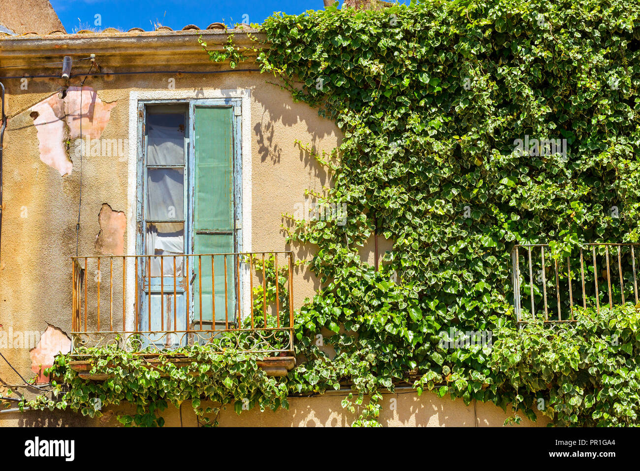 Alte Mauer mit geschmiedeten, Balkon und einer defekten Tür. Grüne Efeu locken auf eine Betonwand. Architektur der Spanischen beach resort Blanes im Sommer. Spanien, Costa Brava, Katalonien Stockfoto