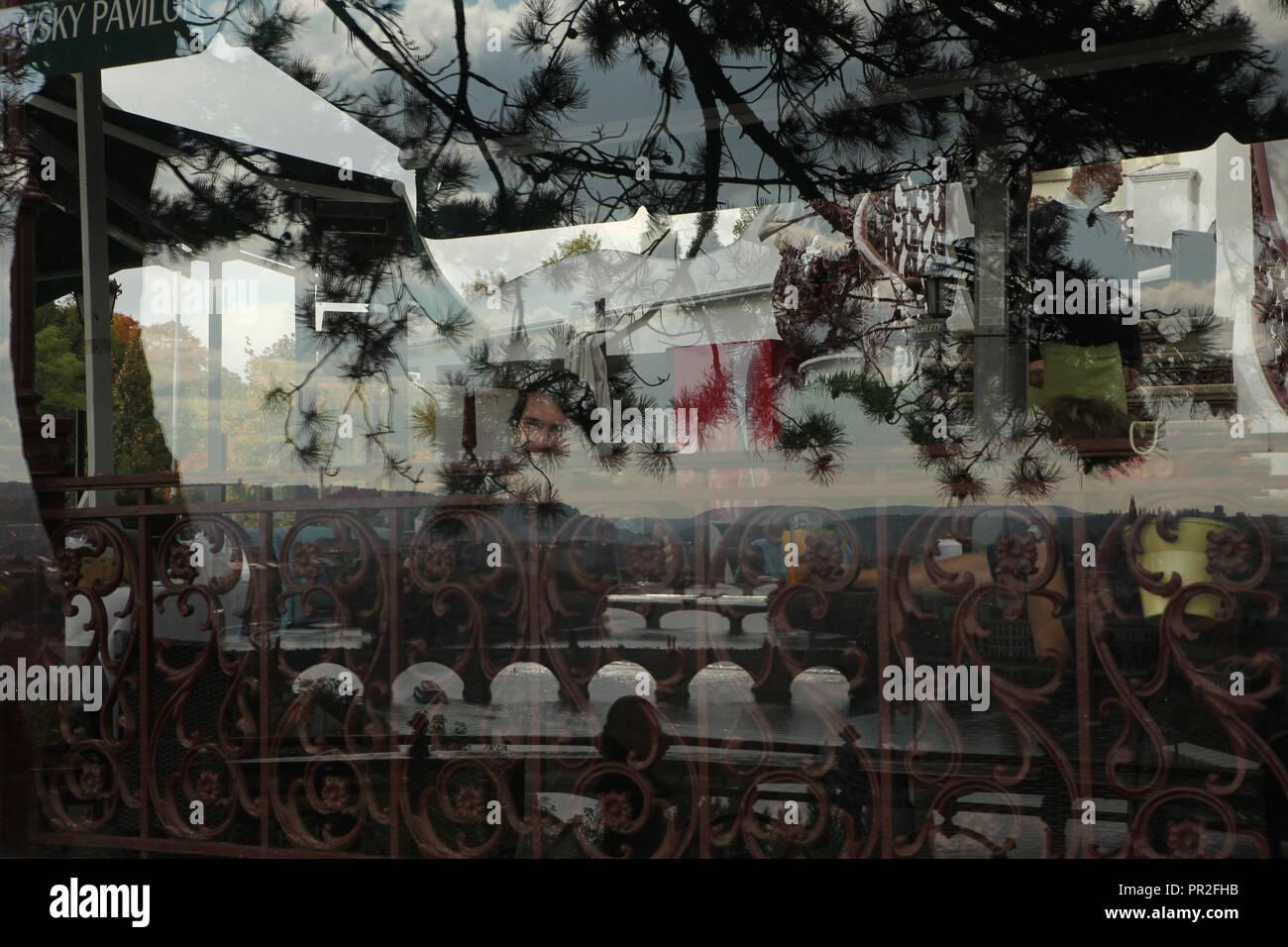 Die Menschen in der Hanavský Pavilon Restaurant in Letná Park (letenské Sady) in Prag, Tschechische Republik, dargestellt durch die Reflexion einer Kiefer und Brücken über die Moldau im Restaurant Fenster. Stockfoto